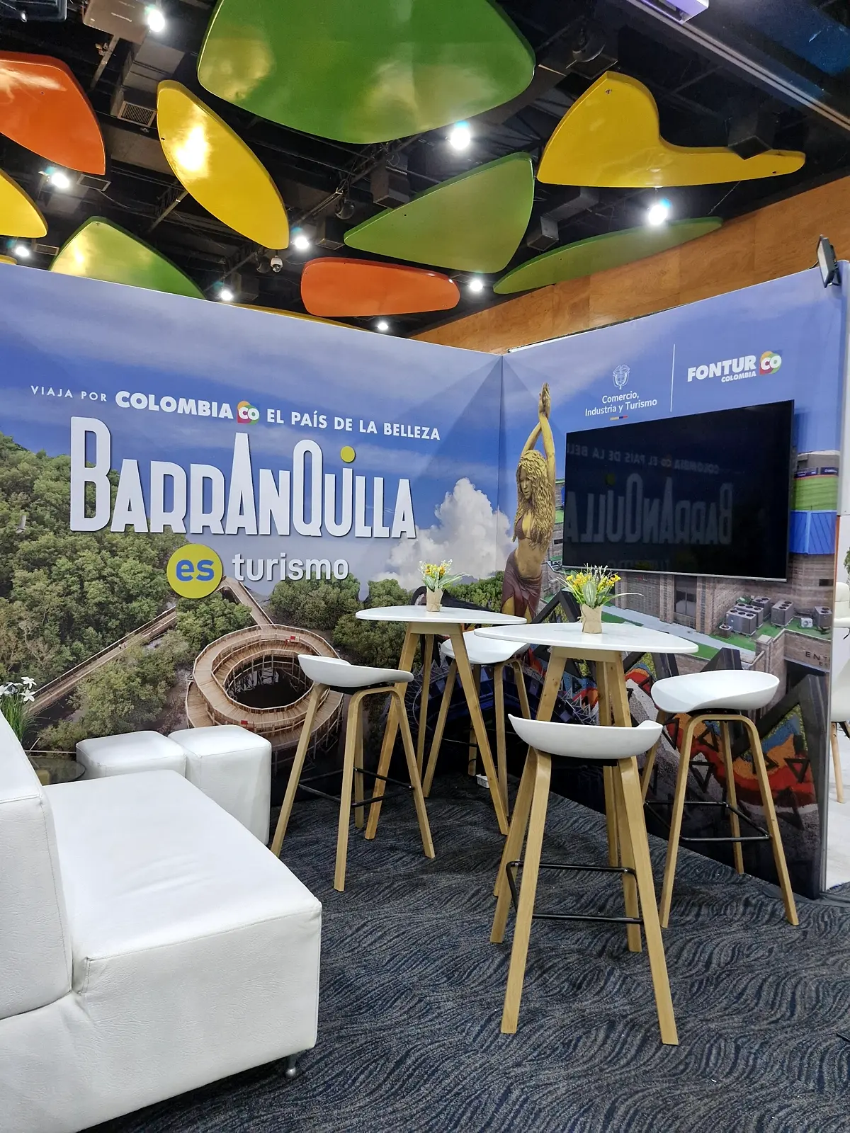 Vista en diagonal del stand con el muro de la pantalla, la escultura impresa en la gráfica y los logos de Comercio, Industria y Turismo y Fontur