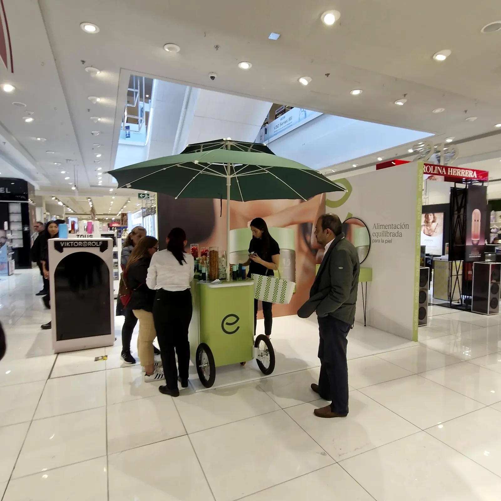 Clientes y asesora junto al carrito de Equilibre frente al backing en L en la zona de belleza de Falabella