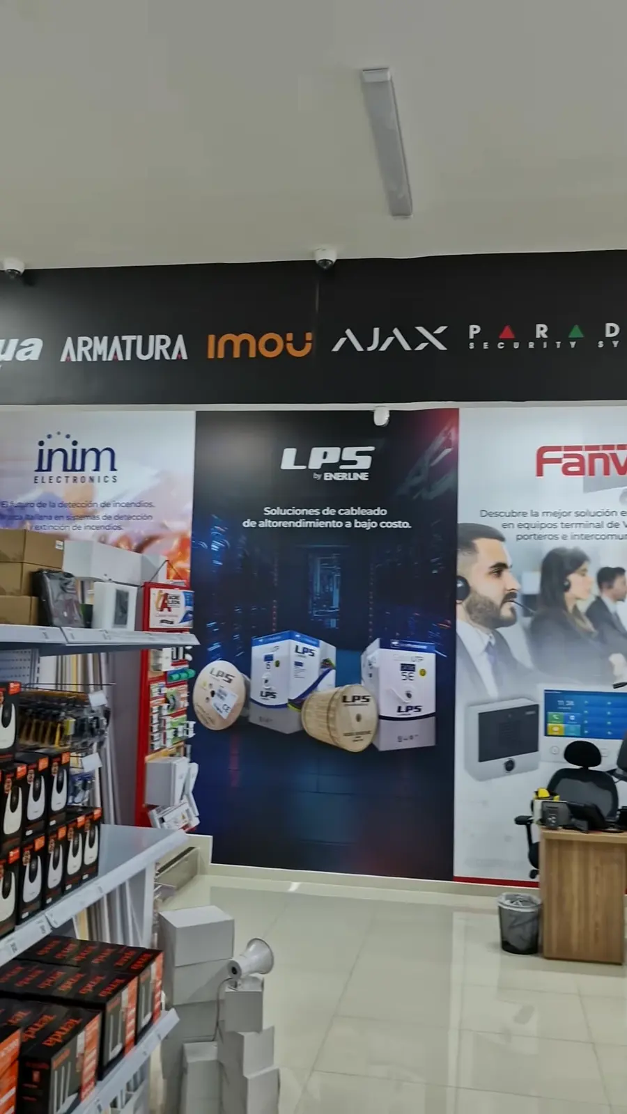Pared de la tienda GVS en vinilo: franja negra con logos de Armatura, Imou, AJAX y Paradox sobre murales de LPS y Fanvil