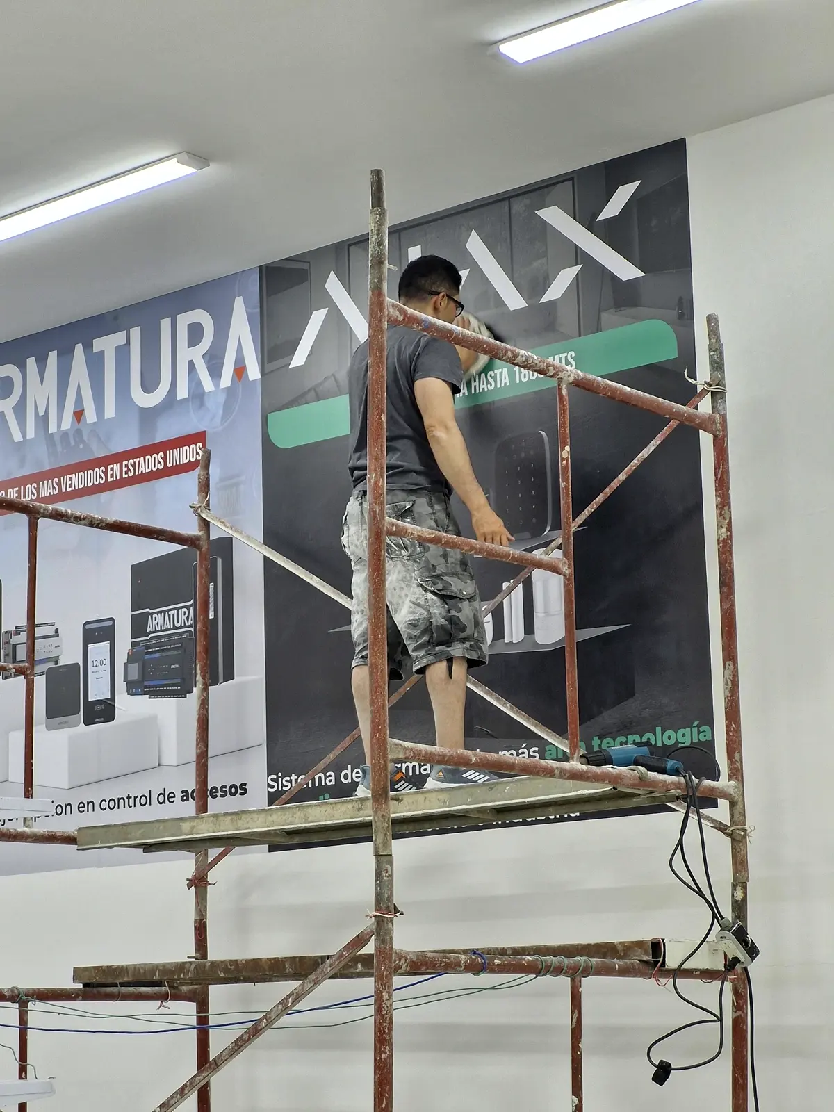 Instalador sobre andamio aplicando el vinilo de los murales Armatura y AJAX en una pared interna de GVS