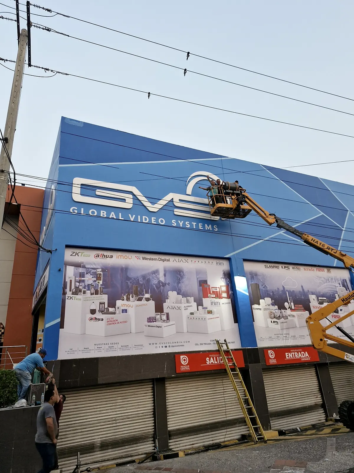 Instaladores en plataforma elevadora fijando el aviso GVS en lo alto de la fachada al amanecer