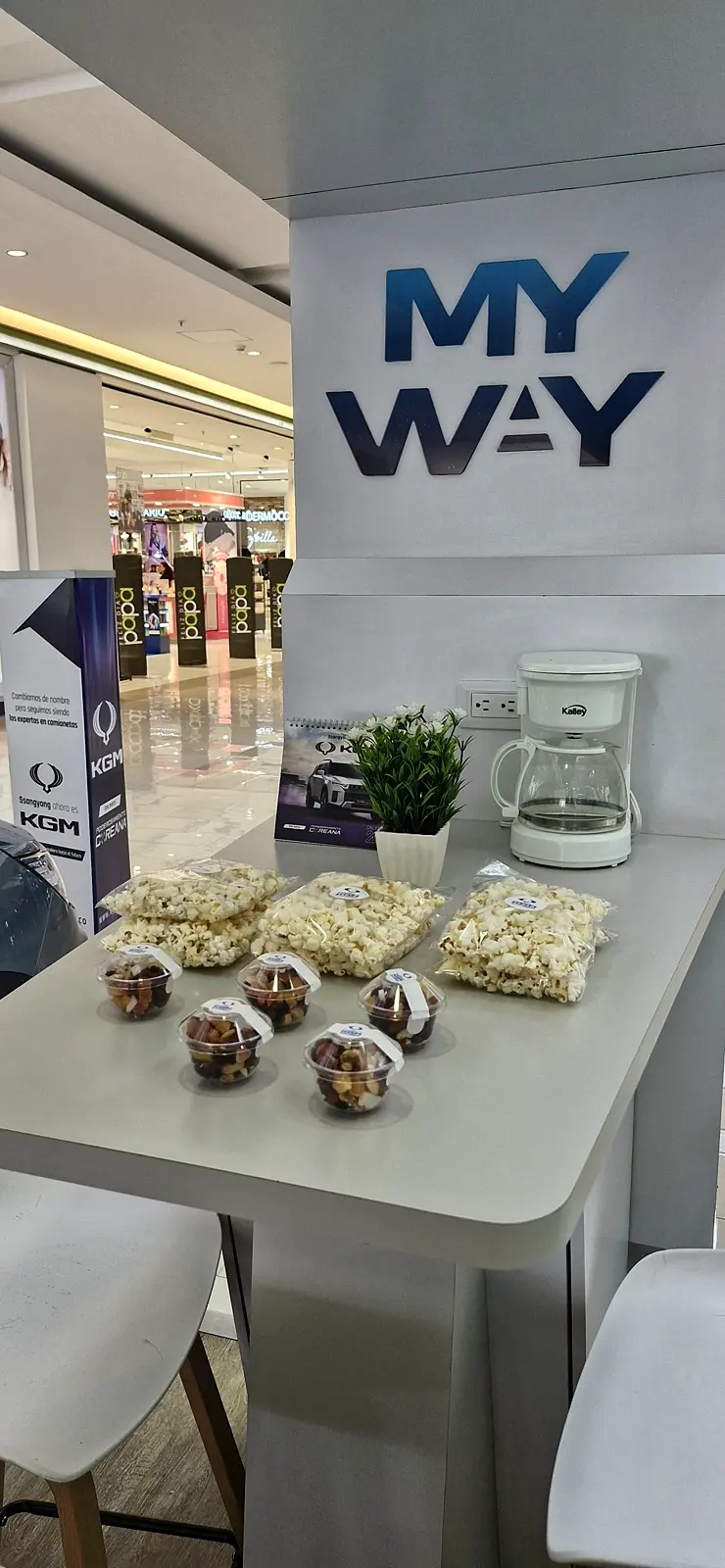Barra del punto KGM con bolsas de crispetas y vasos de pasabocas con etiqueta de marca, matera y roll-up KGM al lado