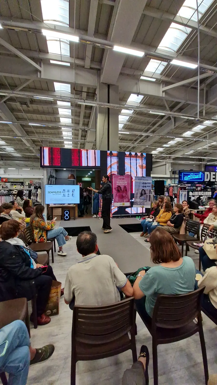 Pasarela negra en U en el piso de venta de un almacén de Bogotá, con pantalla LED al fondo y público sentado alrededor durante el conversatorio de Lilipink