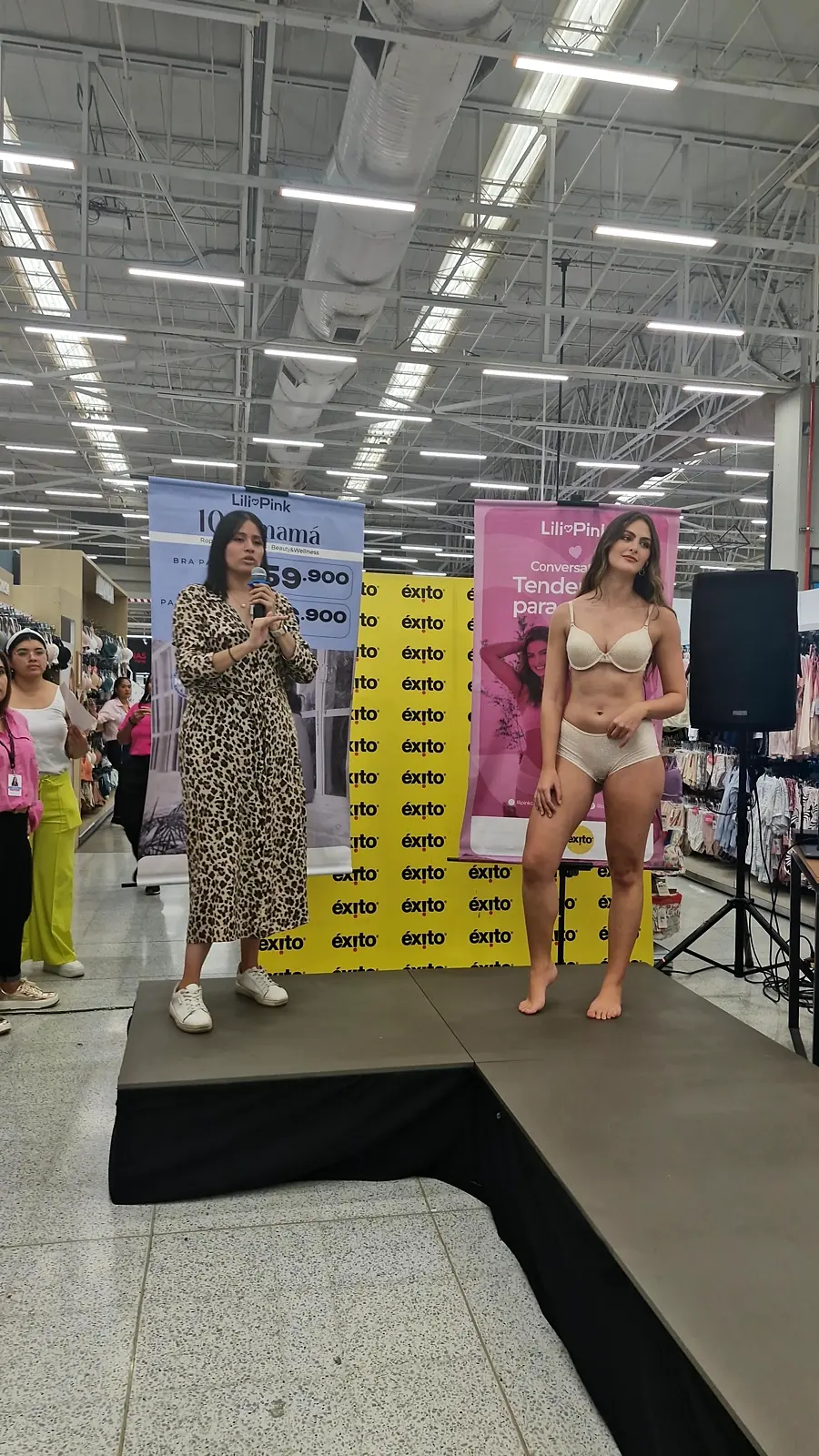 Presentadora con micrófono y modelo sobre la pasarela, con los pendones de Lilipink al fondo, durante el conversatorio en Barranquilla