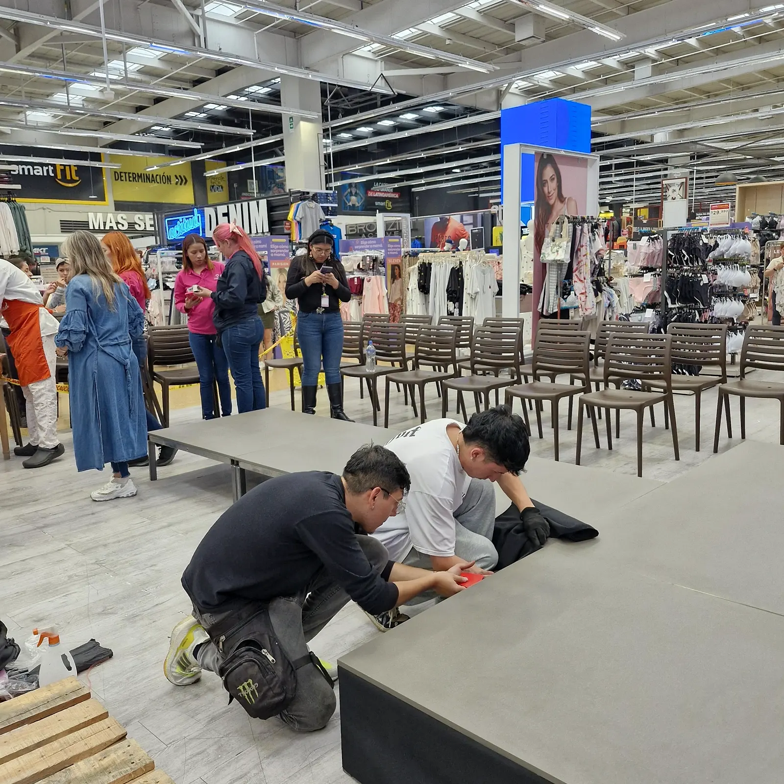 Dos montajistas instalando el faldón negro de la pasarela modular en el piso de venta, con las sillas del público ya ubicadas