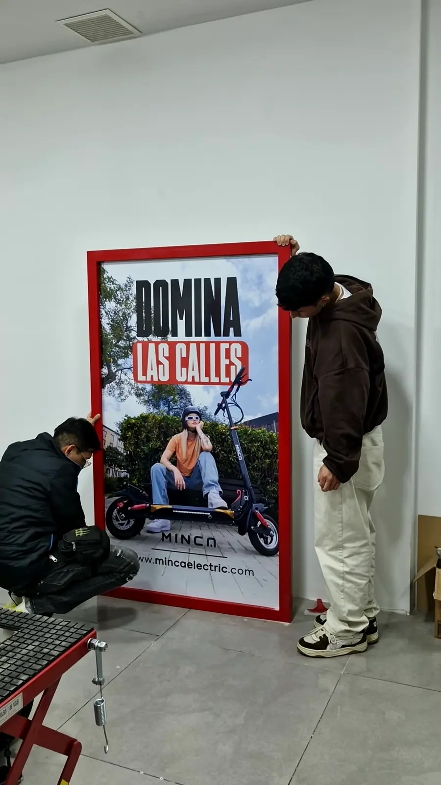 Tótem de marco rojo terminado, apoyado en la pared mientras dos personas revisan los últimos detalles