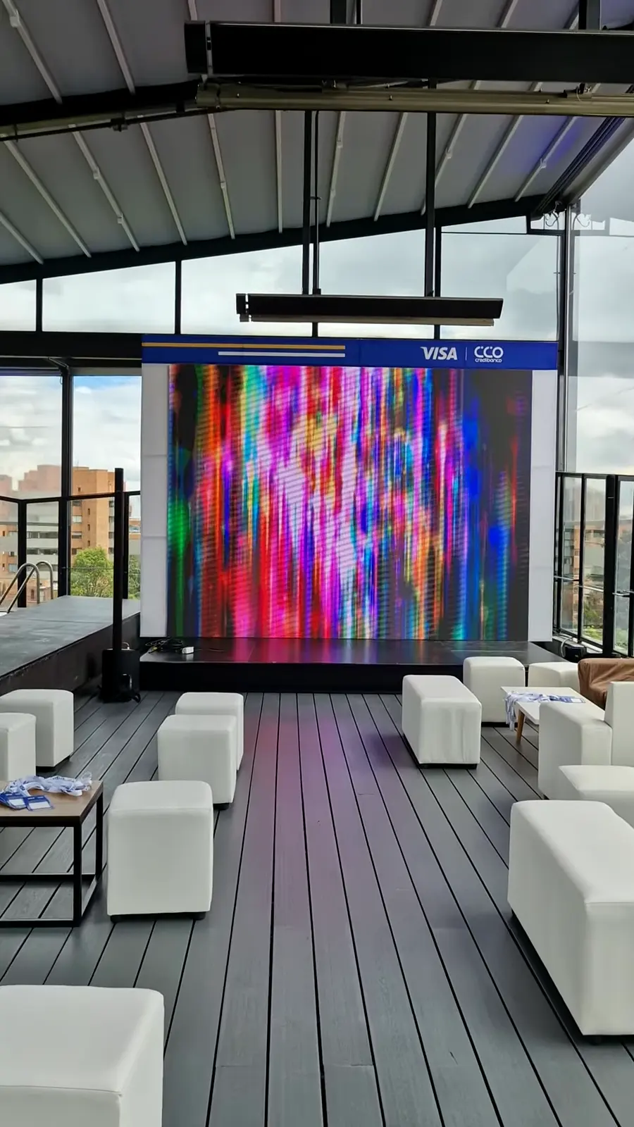 Terraza con mobiliario lounge blanco frente a una pantalla LED enmarcada por un arco con cabezote azul de Visa y Credibanco