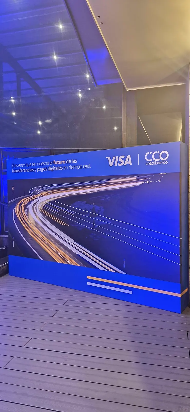 Backing de Visa y Credibanco con gráfica de estelas de luz, de noche bajo luces azules en la terraza